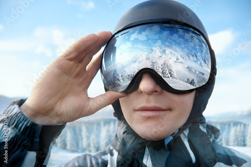 Close Up Of The Ski Goggles Of A Man With The Reflection Of Snowed Mountains. Man On The Background Blue Sky. Wearing Ski Glasses. Winter Sports