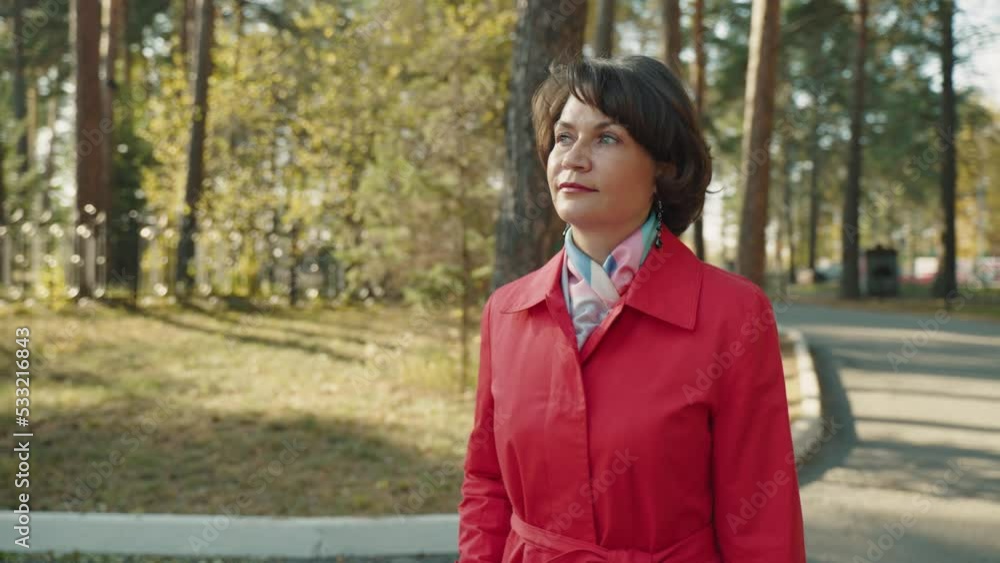 A woman in a red raincoat walks through a beautiful country park in the autumn. A walk through the forest. Slender brunette against a background of golden foliage. A warm sunny day. Slow motion. A woman in a red raincoat walks through a beautiful country park in the autumn. A walk through the forest. Slender brunette against a background of golden foliage. A warm sunny day. Slow motion.