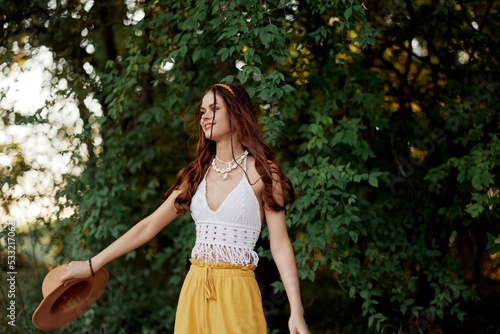 A woman in eco-friendly clothing in a hippie look dances in nature in the park and smiles at the world. The concept of harmony with the body and the surrounding nature