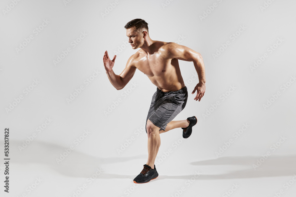Fototapeta premium Handsome muscular man with perfect torso running against white background