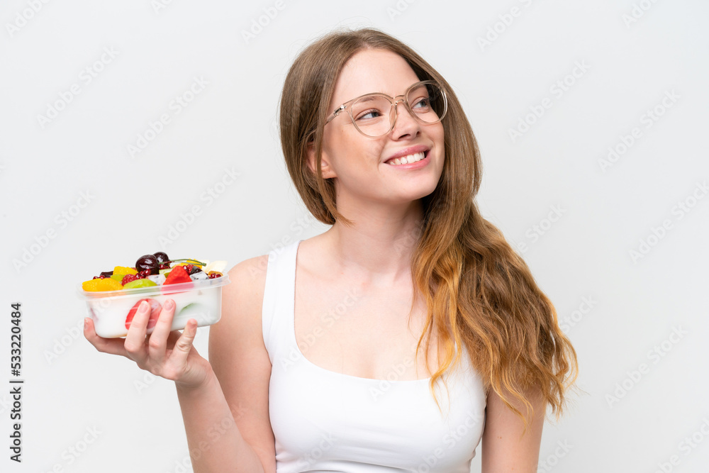 Young pretty woman holding a bowl of fruit isolated on white background looking up while smiling Young pretty woman holding a bowl of fruit isolated on white background looking up while smiling