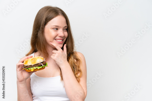 Young pretty woman holding a burger isolated on white background thinking an idea and looking side