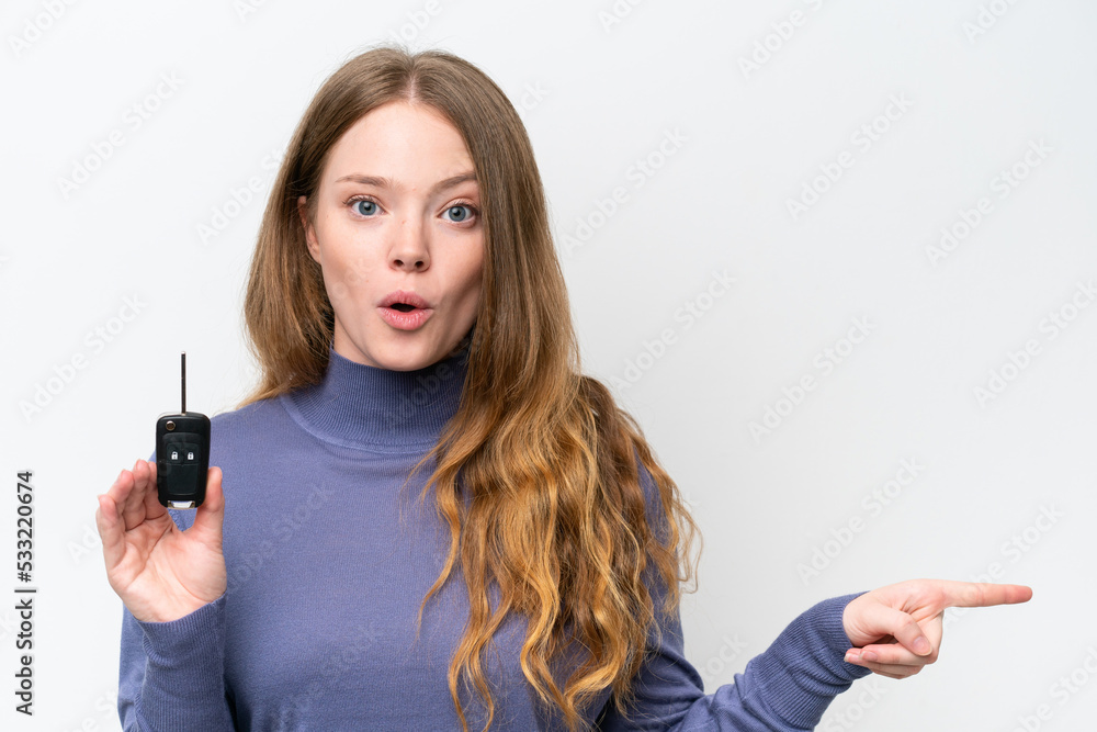 Young caucasian woman holding car keys isolated on white background surprised and pointing side Young caucasian woman holding car keys isolated on white background surprised and pointing side