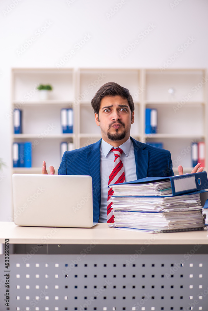 Young male employee unhappy with excessive work in the office Young male employee unhappy with excessive work in the office