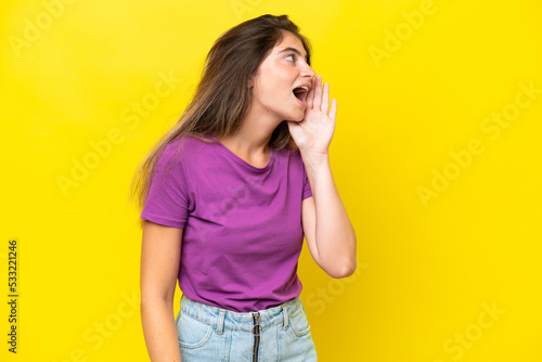 Young caucasian woman isolated on yellow background shouting with mouth wide open to the side