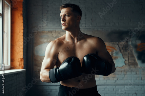 Confident young man in boxing gloves looking away while standing in gym
