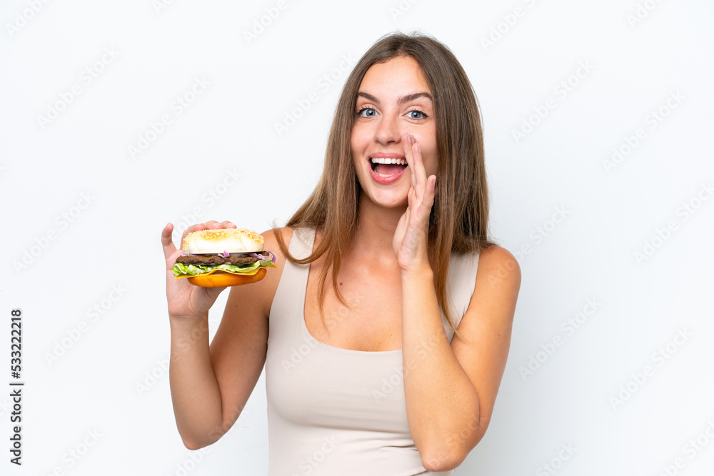 Young pretty woman holding a burger isolated on white background shouting with mouth wide open
