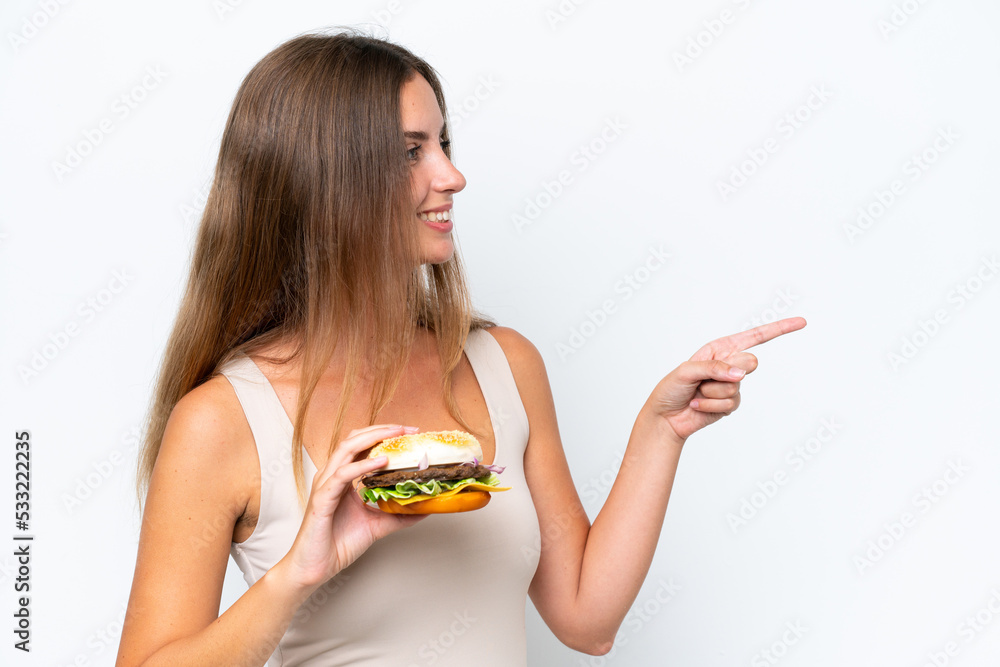 Young pretty woman holding a burger isolated on white background pointing to the side to present a product Young pretty woman holding a burger isolated on white background pointing to the side to present a product