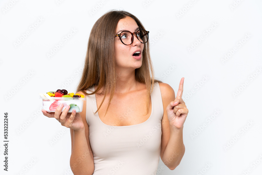 Young pretty woman holding a bowl of fruit isolated on white background intending to realizes the solution while lifting a finger up Young pretty woman holding a bowl of fruit isolated on white background intending to realizes the solution while lifting a finger up