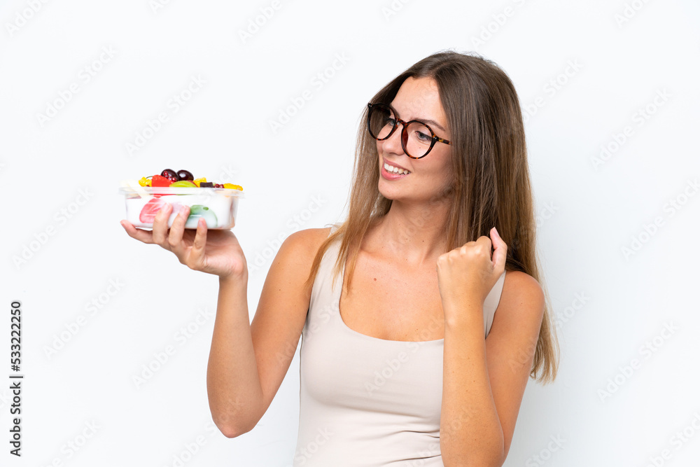 Young pretty woman holding a bowl of fruit isolated on white background celebrating a victory Young pretty woman holding a bowl of fruit isolated on white background celebrating a victory