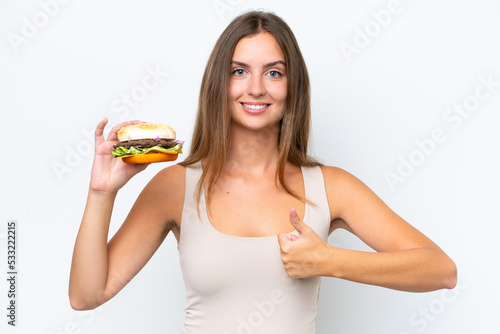 Young pretty woman holding a burger isolated on white background with thumbs up because something good has happened