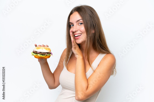Young pretty woman holding a burger isolated on white background whispering something