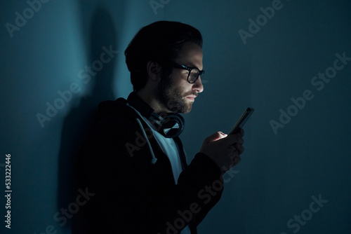 Confident young man using smart phone in the dark