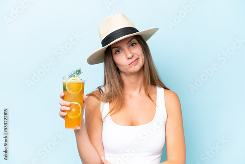 Young beautiful woman holding a cocktail isolated on blue background with sad expression