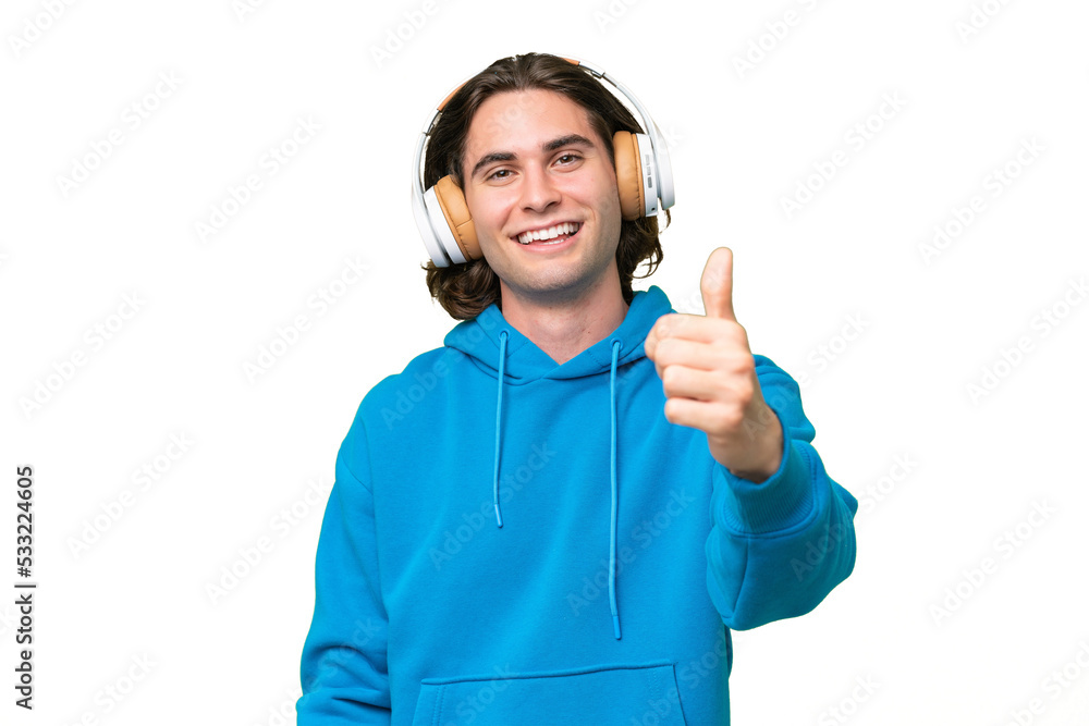 Young handsome man isolated on green chroma background listening music and with thumb up