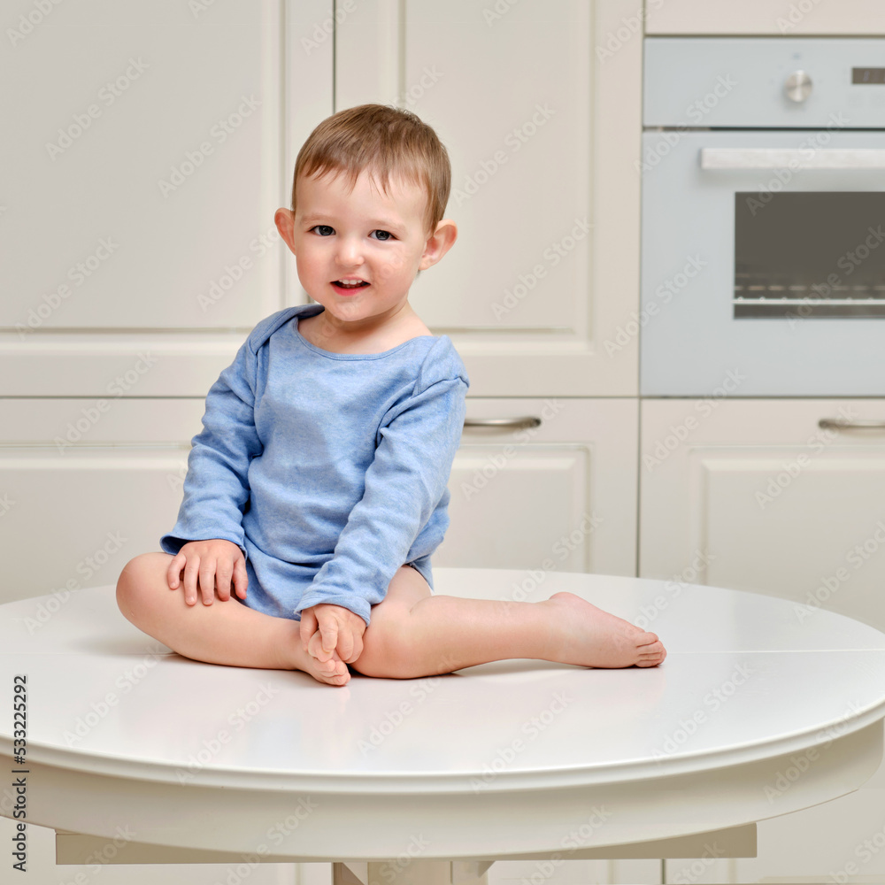 Toddler baby climbed on the kitchen white table. A child in danger climbed to the top, risking falling off the furniture. Kid aged one year and two months Toddler baby climbed on the kitchen white table. A child in danger climbed to the top, risking falling off the furniture. Kid aged one year and two months