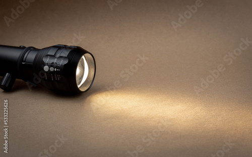 A bright beam of light from a flashlight shines on a brown recycled craft paper background. Old grunge vintage highly textured paper background