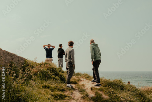 group of boys from behind on a wild cliff while looking at the sea at the horizon during a surf and travel week experience in Somo, Cantabria (Spain)