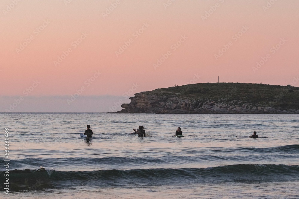 group of surfers in the sea with the board while waiting for the arrival of the waves at sunset during a surf and travel week experience in Somo, Cantabria (Spain)