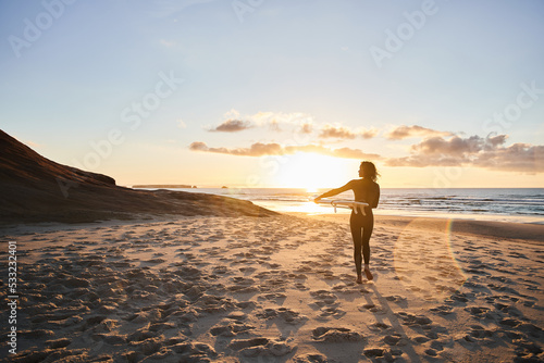 Woman wearing protective wetsuit walking through the beach with surfboard
