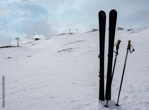 Mountain skis and ski sticks on bright alpine snow on background of mountain slope and a cloundy sky. Winter holidays. Extreme sport. Vacation, travel content. Copy space