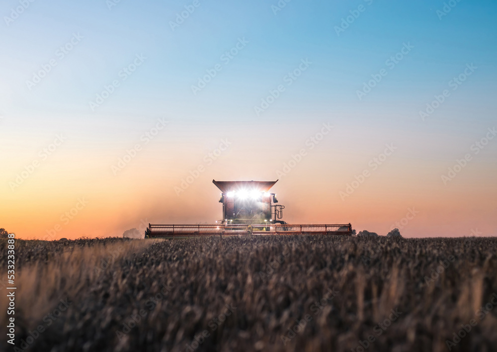 Combine harvester with front headlights illuminating the field at dusk