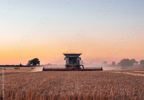 Obraz na płótnie Combine harvester working in a wheat field at sunset w salonie