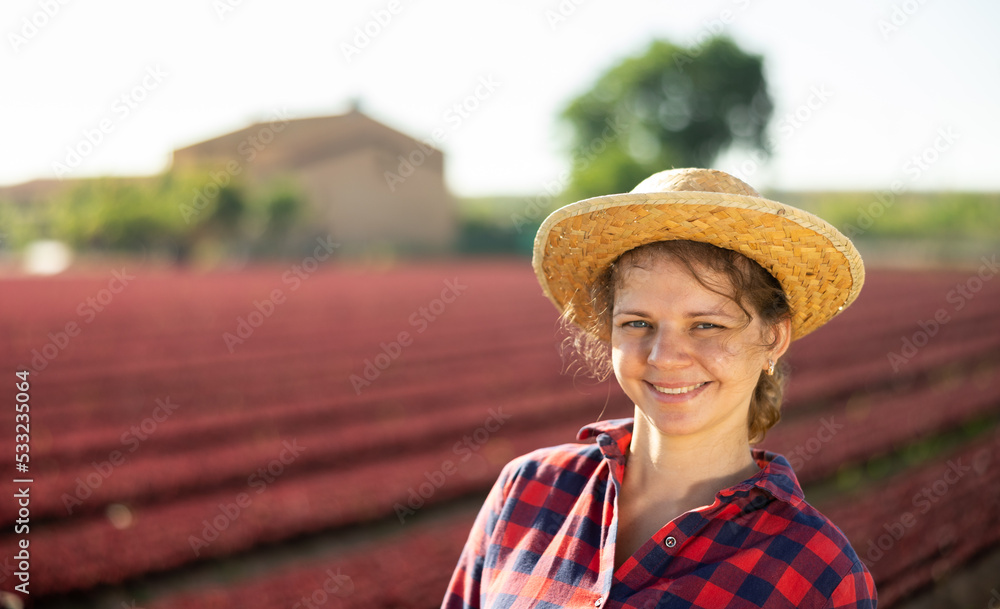 Portrait of young smiling girl farm worker wearing plaid shirt and wicker straw hat standing on vegetable field 