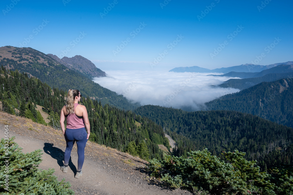Young woman hiking on Hurricane Ridge trail in Olympic National Park, Washington observes cloud inversion on sunny autumn afternoon.