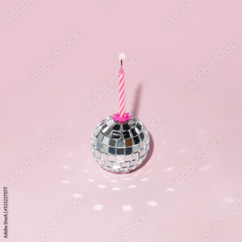 Shiny disco ball and candle on pastel light pink background. Minimalistic party concept. Creative birthday composition.