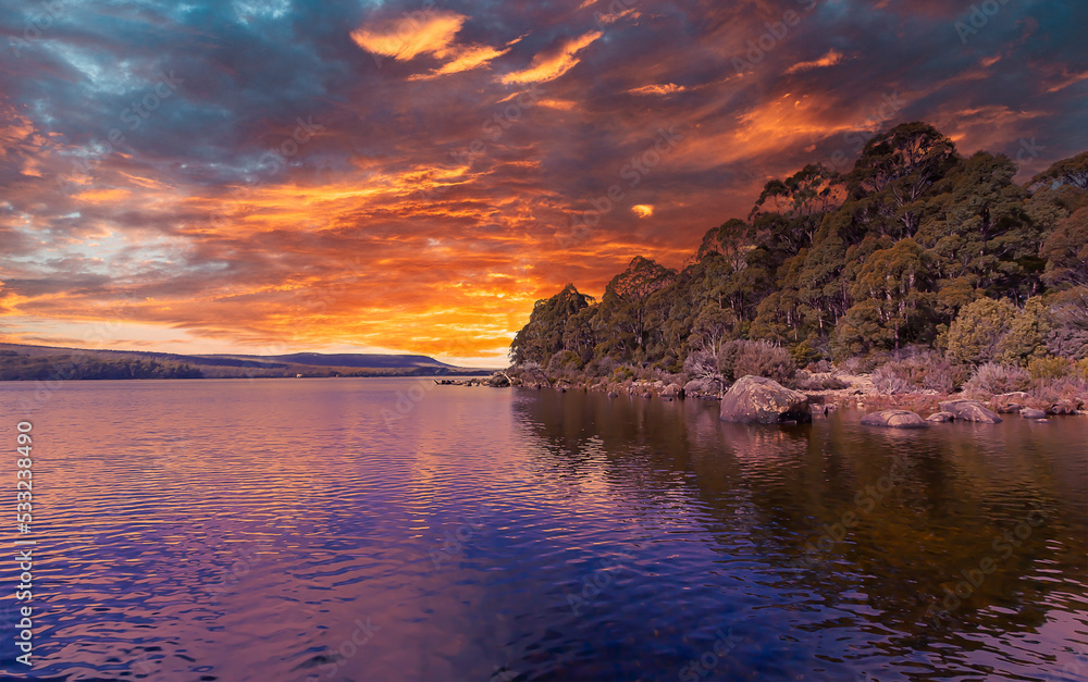 A spectacular cloudy colourful sunset sky is reflected and highlighted in the water and landscape of this natural coastal scene in Tasmania, Australia.