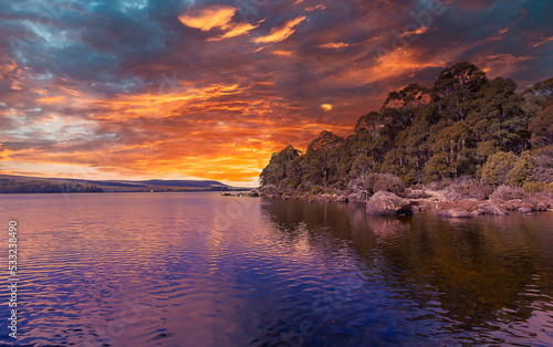 A spectacular cloudy colourful sunset sky is reflected and highlighted in the water and landscape of this natural coastal scene in Tasmania, Australia.