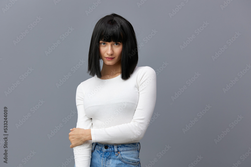 a relaxed woman is standing full-face on a dark background in a white tight T-shirt, calmly standing holding the other with one hand a relaxed woman is standing full-face on a dark background in a white tight T-shirt, calmly standing holding the other with one hand