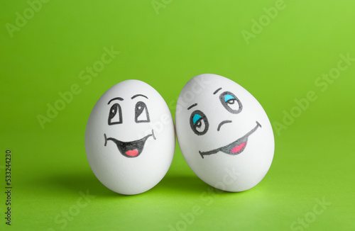 Eggs with drawn happy faces on green background