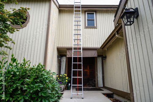 Getting ready for fall home maintenance, tall aluminum extension ladder against a two-story house