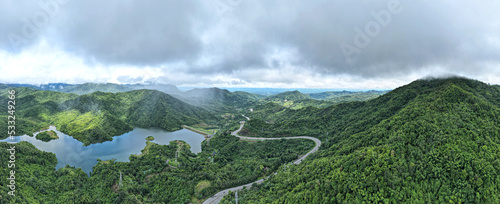Bird's-eye view of a mountain view overlooking the road and mist surrounding mountains, green forests and rivers.
