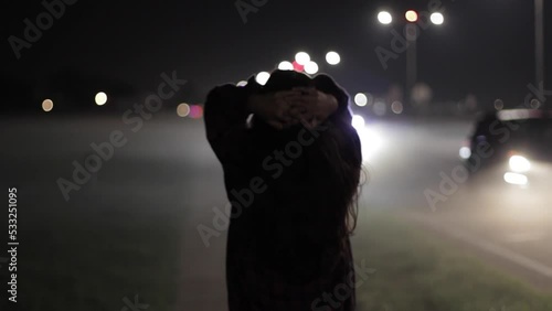 Young Woman Walking Through The Streets At Night Clutching Her Hands Behind Her Head photo