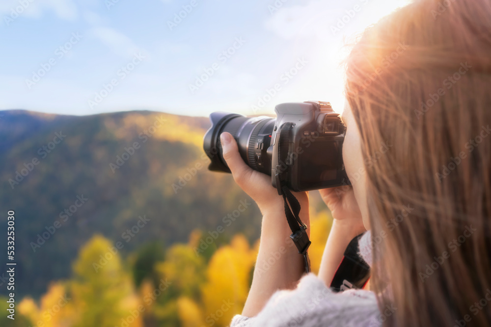 A woman photographer takes pictures of nature with a camera close-up view from the back free space. Autumn travel and active lifestyle.