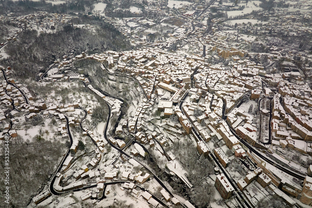 Fototapeta premium Aerial winter landscape of dense historic center of Thiers town in Puy-de-Dome department, Auvergne-Rhone-Alpes region in France. Rooftops of old buildings and narrow streets at snowfall