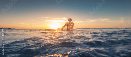 Surfer entering the ocean at sunset © bartsadowski