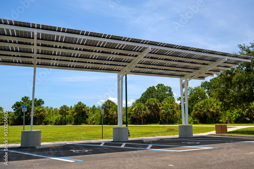 Solar panels installed as shade roof over parking lot for parked electric cars for effective generation of clean electricity. Photovoltaic technology integrated in urban infrastructure
