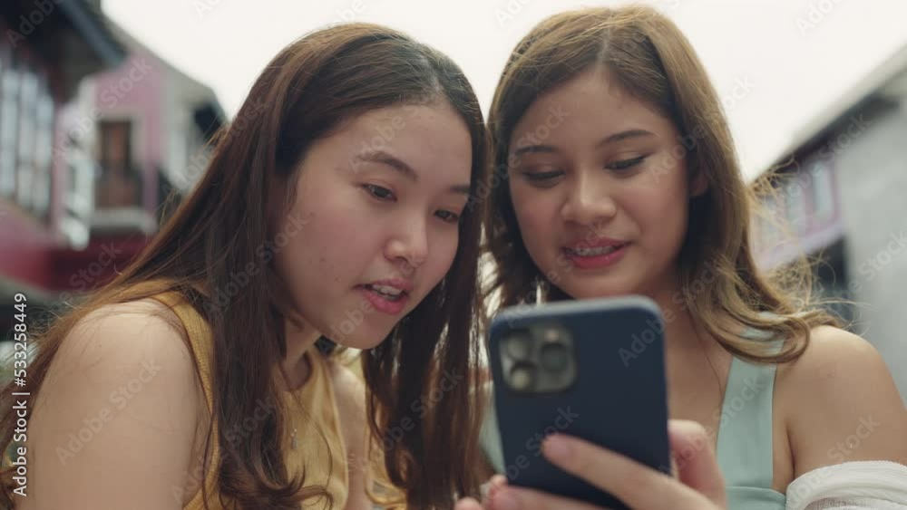 Young Gen Z asia people trending influencer teen girl look at phone enjoy read review and watch viral video laugh joy play social media app post share online fun standing in modern city relax outside. Young Gen Z asia people trending influencer teen girl look at phone enjoy read review and watch viral video laugh joy play social media app post share online fun standing in modern city relax outside.