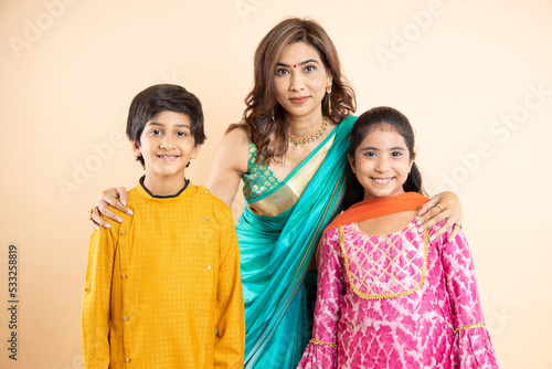 Portrait of Indian mother with kids wearing traditional cloths as they celebrate diwali standing isolated on studio background, Festival or auspicious occasion,
