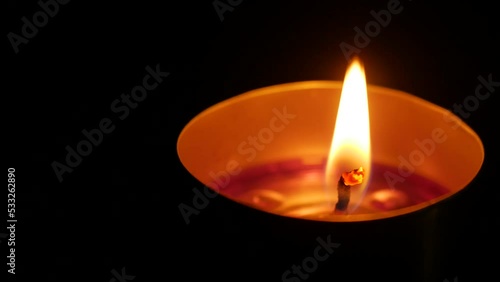 Burning candle at night. Candle flame glowing on a dark background. Close up. Symbol of life, love and light, protection and warmth of the hearth. Copyspace. Lit candle in an aluminum metal cup