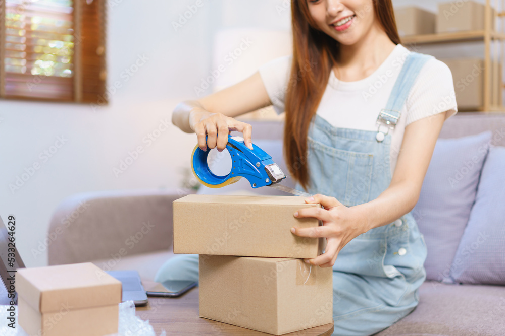 Online merchant concept, Female entrepreneur is packing products and sealing parcel boxes with tape