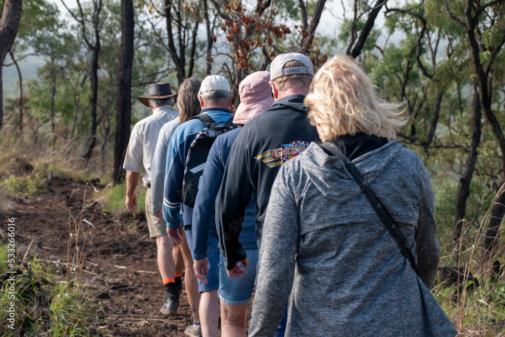 Back view, group of tourists walk single file through Queensland outback Back view, group of tourists walk single file through Queensland outback