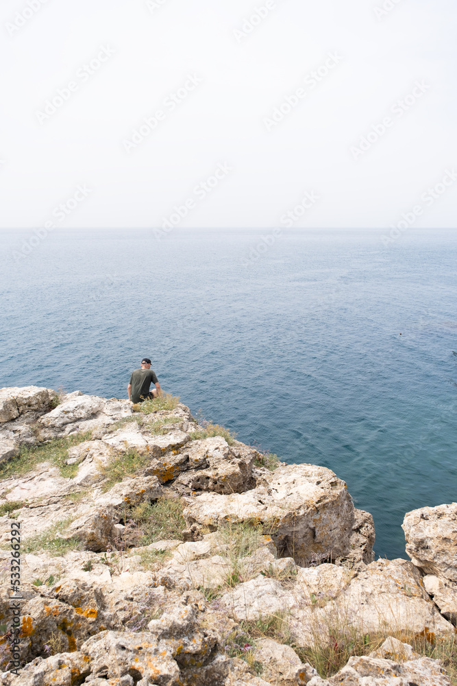 Cape Tarkhankut. A man sits on the edge of a cliff. A man enjoys a vacation by the sea. Crimean peninsula.