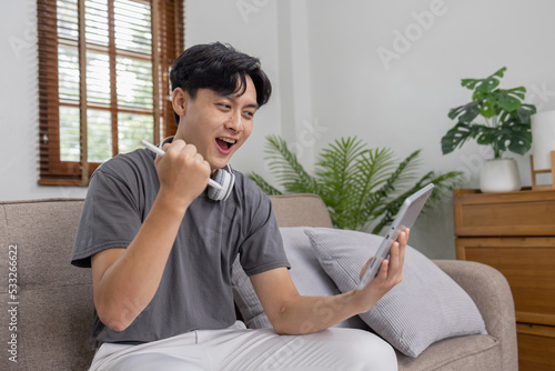 Excited young asian man hold tablet chatting in dating app feel happy sit on sofa at home, Close up joyful male reading good news on phone. Surprised lady celebrating victory on tablet