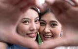 Young Asian lesbian couple in a romantic mood making heart-shaped hand gesture. LGBT couple showing love and affection while playing with camera in home setting.