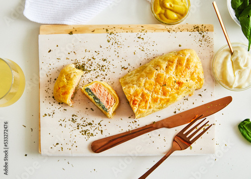 Salmon strudel with spinach, served on wood board, white background with setting and ingredient photo